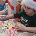 Chłopiec maluje drewnianą lokomotywę farbami.