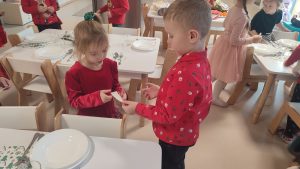 Dzieci w strojach świątecznych dzielą się opłatkiem i składają sobie życzenia.