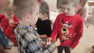 Dzieci w strojach świątecznych dzielą się opłatkiem i składają sobie życzenia.