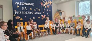 Na zdjęciu dzieci z pasowanych grup siedzące na tle dekoracji "Pasowanie na przedszkolaka"