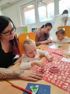 Na zdjęciu widać dzieci z rodzicami podczas pracy warsztatowej - ozdabianie gwiazdki z masy ceramicznej.