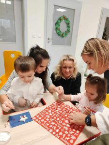 Na zdjęciu widać dzieci z rodzicami oraz panie podczas pracy warsztatowej - ozdabianie gwiazdki z masy ceramicznej.