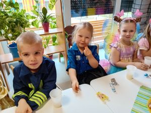 Troje dzieci, chłopiec i dwie dziewczynki siedzą uśmiechnęci przy stoliczu.