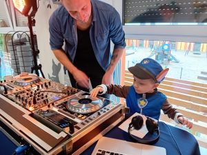 Chłopiec stoi obok DJ i gra na konsoli.