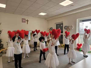 Dzieci tańczą na szarym dywanie w rękach trzymają czerwone serca.