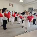 Dzieci tańczą na szarym dywanie w rękach trzymają czerwone serca.