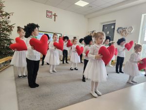 Dzieci tańczą na szarym dywanie w rękach trzymają czerwone serca.