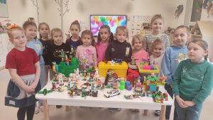 Dziewczynki stoją obok siebie. Przed nimi stolik na którym położone są budowle z klocków LEGO.