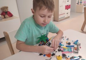 Chłopiec przy stoliku tworzy budowle z klocków LEGO.