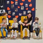 Dzieci siedzą na krzesełkach, w tle dekoracja i