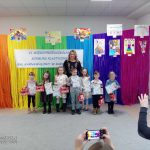 Pani dyrektor przedszkola pozuje do zdjęcia razem z dziećmi na tle kolorowej tęczy.