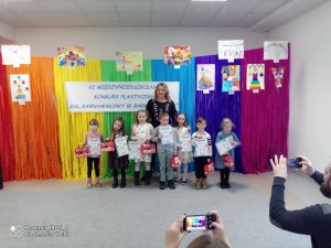 Pani dyrektor przedszkola pozuje do zdjęcia razem z dziećmi na tle kolorowej tęczy.