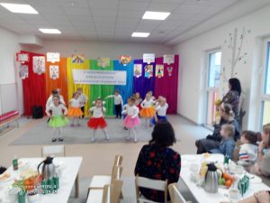 Grupa dzieci występuje na tle tęczowej ściany.