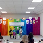 Grupa dzieci występuje na tle tęczowej ściany.