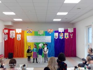 Grupa dzieci występuje na tle tęczowej ściany.