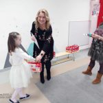 Pani dyrektor przedszkola wręcza dyplom i nagrodę dziewczynce ubranej na biało.