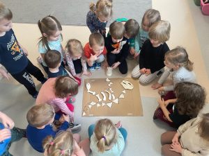 Dzieci siedzą w kole i oglądają kości dinozaura