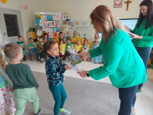 Pani dyrektor Izabela ubrana w zielony sweter i kolorowe skarpetki wręcza dziewczynce dyplom i nagrodę.