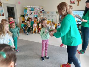 Pani dyrektor Izabela ubrana w zielony sweter i kolorowe skarpetki wręcza dziewczynce dyplom i nagrodę.