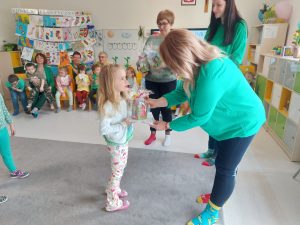 Pani dyrektor Izabela ubrana w zielony sweter i kolorowe skarpetki wręcza dziewczynce dyplom i nagrodę.