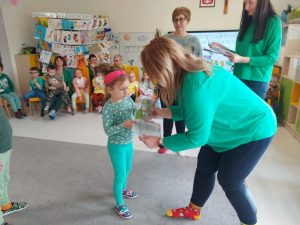 Pani dyrektor Izabela ubrana w zielony sweter i kolorowe skarpetki wręcza dziewczynce dyplom i nagrodę.