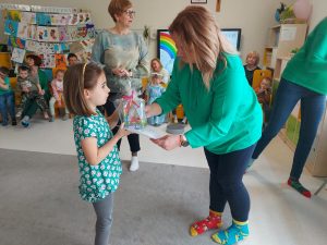 Pani dyrektor Izabela ubrana w zielony sweter i kolorowe skarpetki wręcza dziewczynce dyplom i nagrodę.