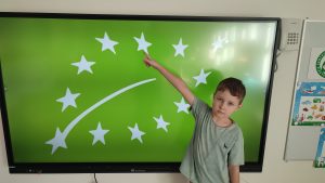 Chłopiec na tablicy multimedialnej pokazuje znaczek produktów ekologicznych.