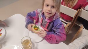 Dziewczynka trzyma w ręce kolorową kanapkę z produktów ekologicznych.