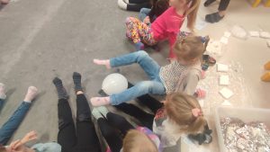 Dzieci nóżkami podają sobie zimny balonik. Są również dzieci niepełnosprawne.