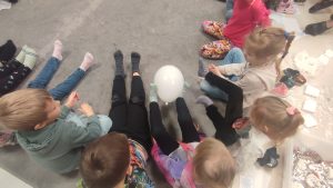 Dzieci nóżkami podają sobie zimny balonik. Są również dzieci niepełnosprawne.