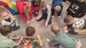 Dzieci paluszkami zbierają z szarego dywanu małe okruszki.