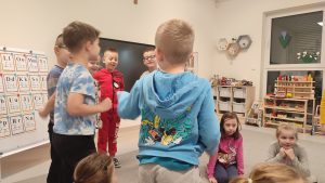 Chłopcy w kolorowych bluzach stoją plecami na szarym dywanie.