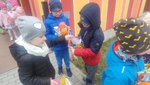 Dzieci wokół przedszkola na trawie szukają i znajdują koszyczki z prezentami.