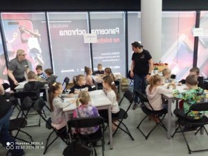 Dzieci kolorują kolorowanki ekologiczne przy czarnych stolikach.