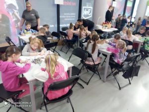 Dzieci kolorują kolorowanki ekologiczne przy czarnych stolikach.