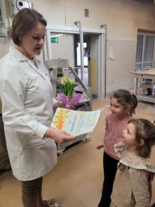 Dwie dziewczynki częstują się ciasteczkami podawanymi przez pracownicę piekarni