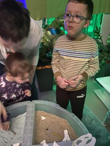 Dzieci z pomocą opiekuna odkopują kości dinozaura.