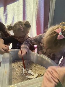 Dzieci z pomocą opiekuna odkopują kości dinozaura.