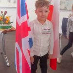 Chłopiec w białej koszuli stoi pomiędzy flagą Polski i Wielkiej Brytanii.