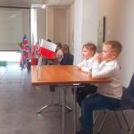 Dwóch chłopców w białych koszulach przy stole z flagą Wielkiej Brytanii rozwiązuje zadania.