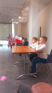 Dwóch chłopców w białych koszulach przy stole z flagą Wielkiej Brytanii rozwiązuje zadania.
