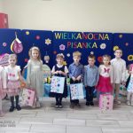 Grupa laureatów stoi z dyplomami i nagrodami na tle granatowej dekoracji z pisankami.