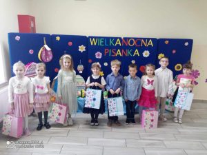 Grupa laureatów stoi z dyplomami i nagrodami na tle granatowej dekoracji z pisankami.