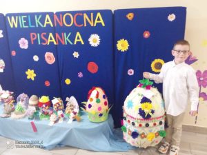 Chłopiec na tle niebieskiej dekoracji i konkursowych pisanek pozuje do zdjęcia.
