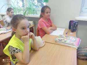 Dwie dziewczynki siedzą w szkolnej ławce. Jedna ma żółtą kamizelkę.