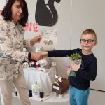 Chłopiec otrzymuje gratulacje, dyplom , roślinkę w doniczce i kostkę Rubika z rąk nauczycielki.