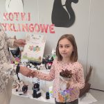 Dziewczynka otrzymuje gratulacje, dyplom , roślinkę w doniczce i kostkę Rubika z rąk nauczycielki.
