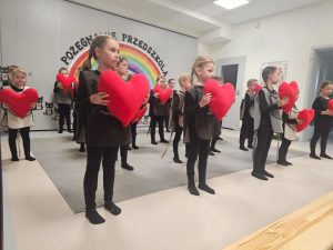 Dzieci ubrane na czarno w kocich kamizelkach przedstawiają program słowno-taneczny na tle tęczy.