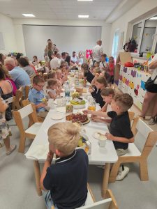 Dzieci siedzą przy białych stolikach i częstują się słodkościami.