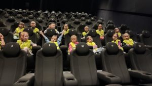 Grupa dzieci w żółtych kamizelkach siedzi na czarnych fotelach w kinie Helios.
